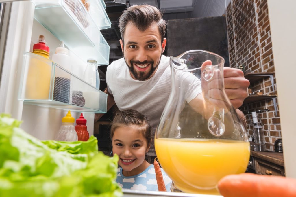 happy young father and adorable daughter taking juice from fridge